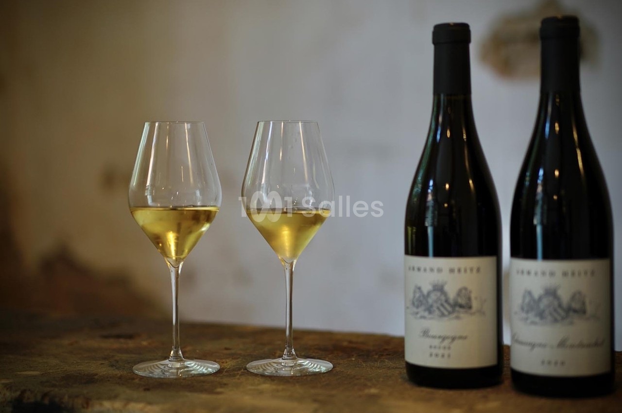 Deux verres de vin blanc et deux bouteilles posés sur une surface en bois, dans un décor sobre et rustique.