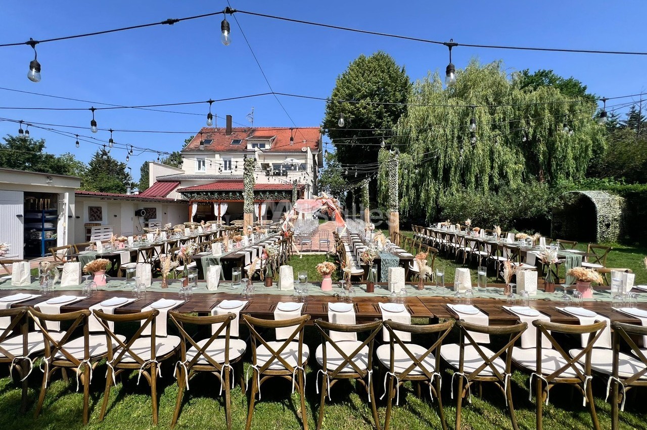Tables décorées pour un mariage en extérieur, disposées en U, avec guirlandes lumineuses et une arche florale au centre.