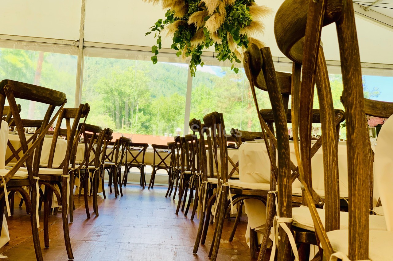 Salle de réception avec des chaises en bois disposées autour de tables, décorée de suspensions végétales.