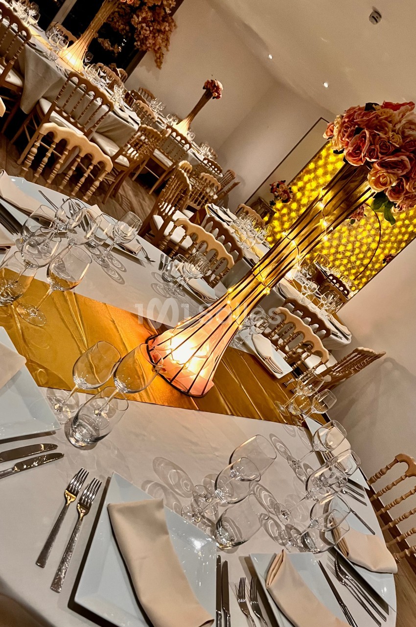 Salle de réception décorée avec des tables rondes, nappes blanches, centres de table fleuris et éclairage chaleureux.