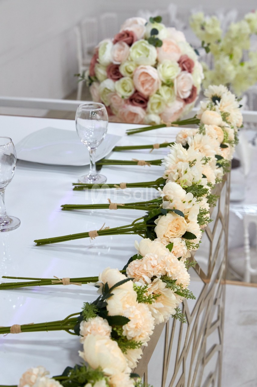 Bouquets de fleurs crème alignés sur une table décorative, avec un centre de table composé de roses pastel en arrière-plan.
