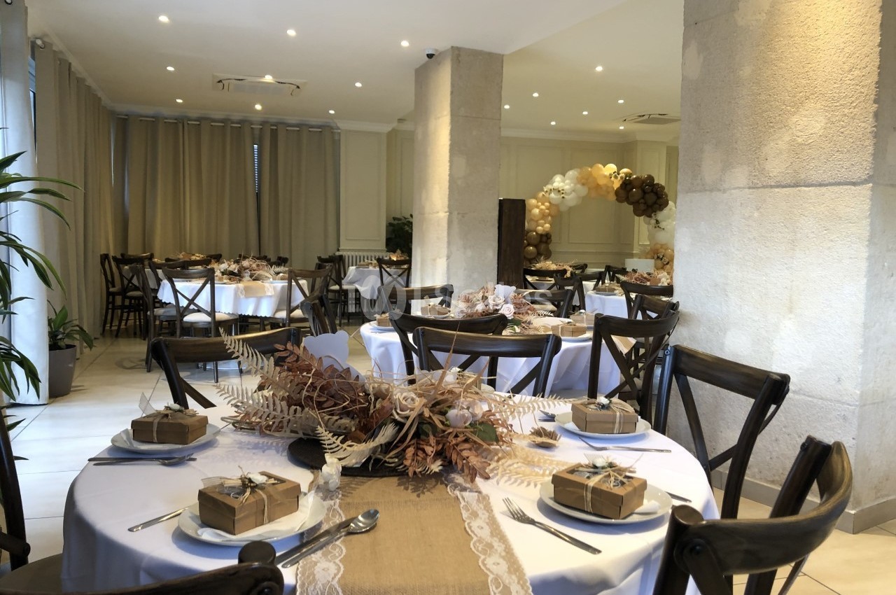 Salle de réception décorée avec des tables rondes, nappes blanches, centres de table floraux et cadeaux emballés.