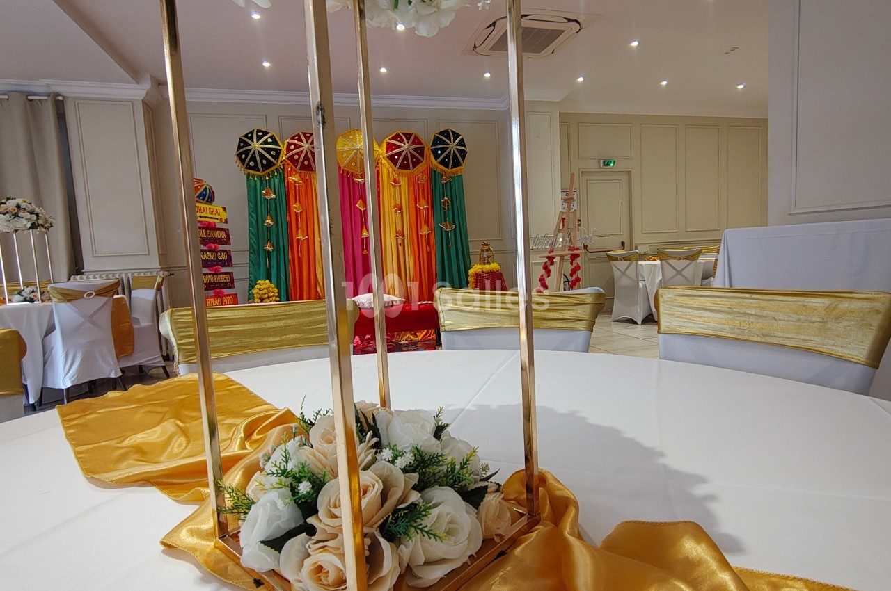 Salle décorée pour un événement avec des chaises dorées, une table ornée de fleurs et un fond coloré.