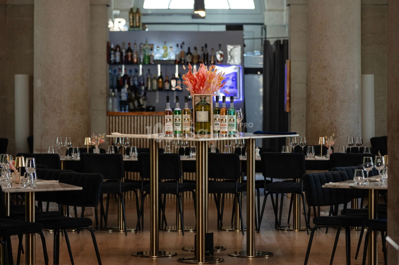 Salle de restaurant élégante avec tables dressées, bar en arrière-plan et fleurs au centre d'une table haute.