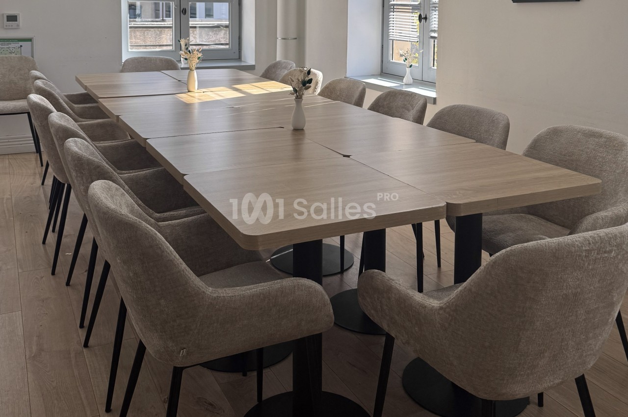 Salle de réunion lumineuse avec une grande table en bois entourée de chaises rembourrées et des vases décoratifs.