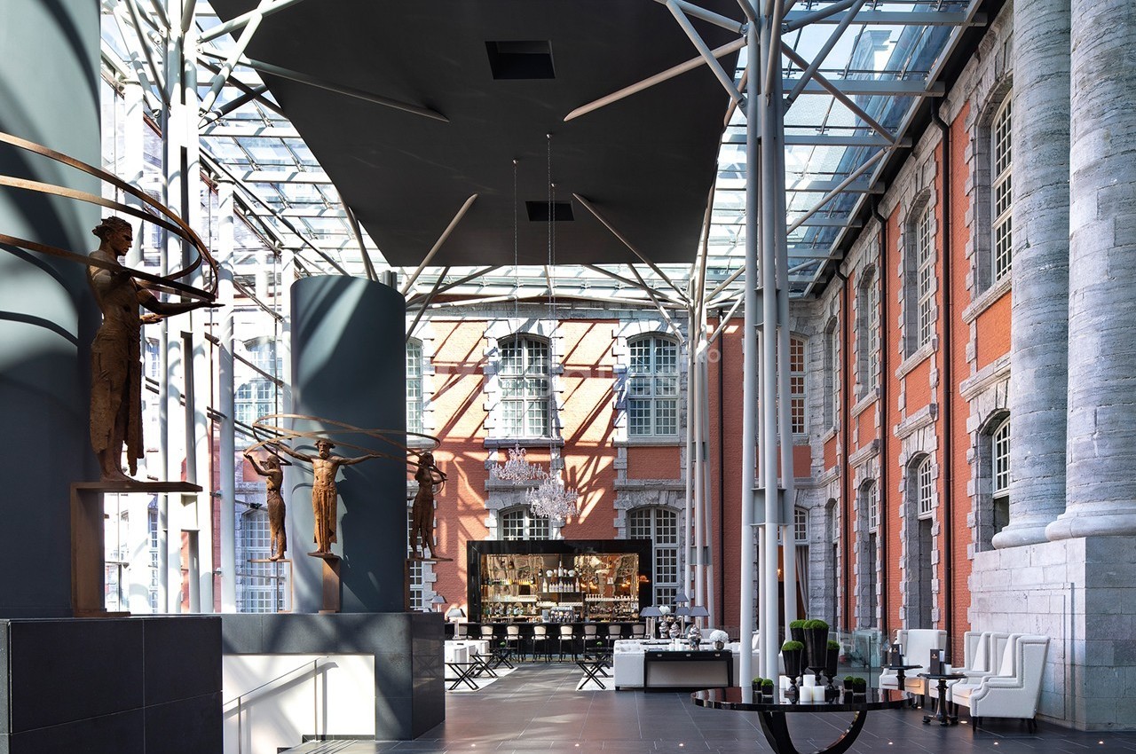 Intérieur d'un bâtiment avec verrière, sculptures modernes, murs en briques rouges et espace aménagé avec tables.