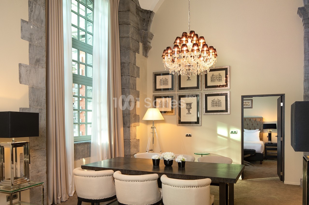 Salle à manger élégante avec table en bois, chaises rembourrées, lustre en cristal et vue sur une chambre adjacente.