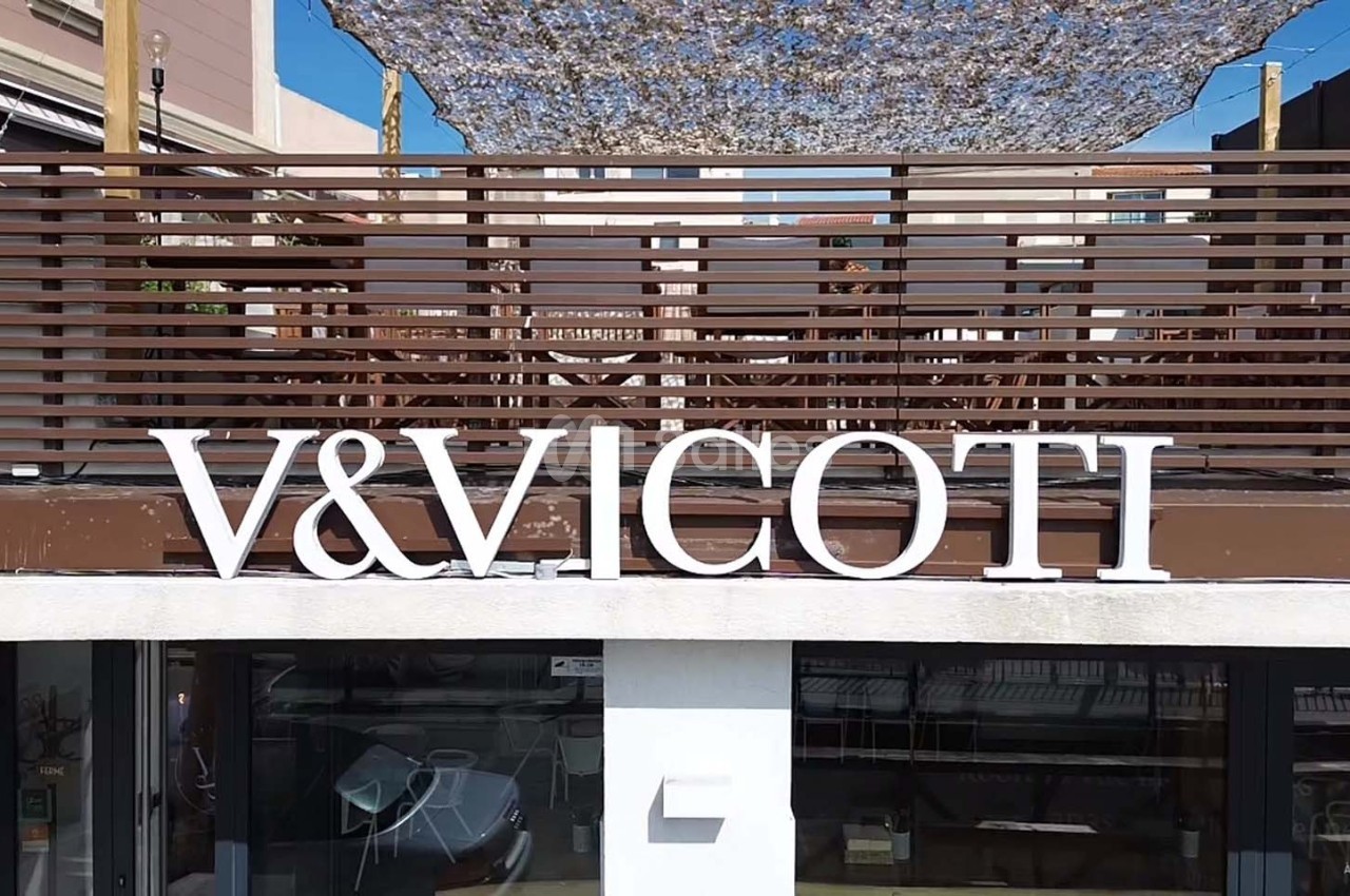 Façade d'un bâtiment avec une enseigne ’V&VICOTI’ en lettres blanches, terrasse en bois et mobilier visible en arrière-plan.