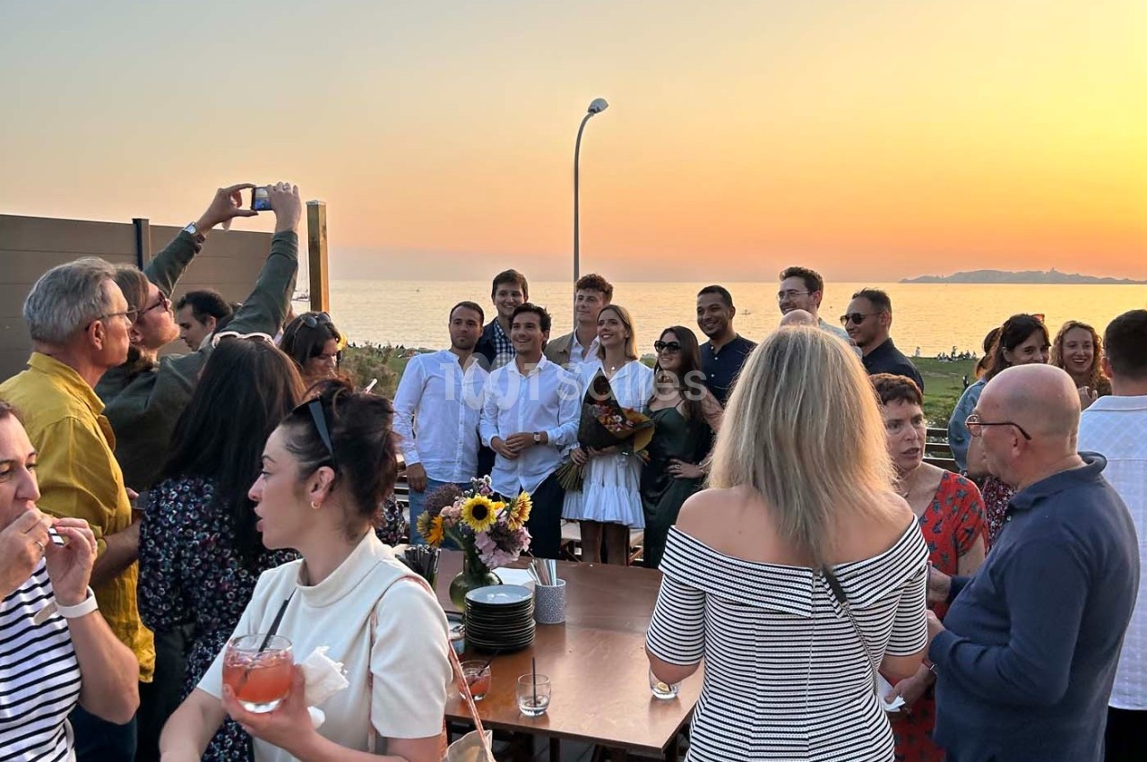 Groupe de personnes réunies en extérieur au coucher du soleil, certaines posant pour une photo, ambiance conviviale.