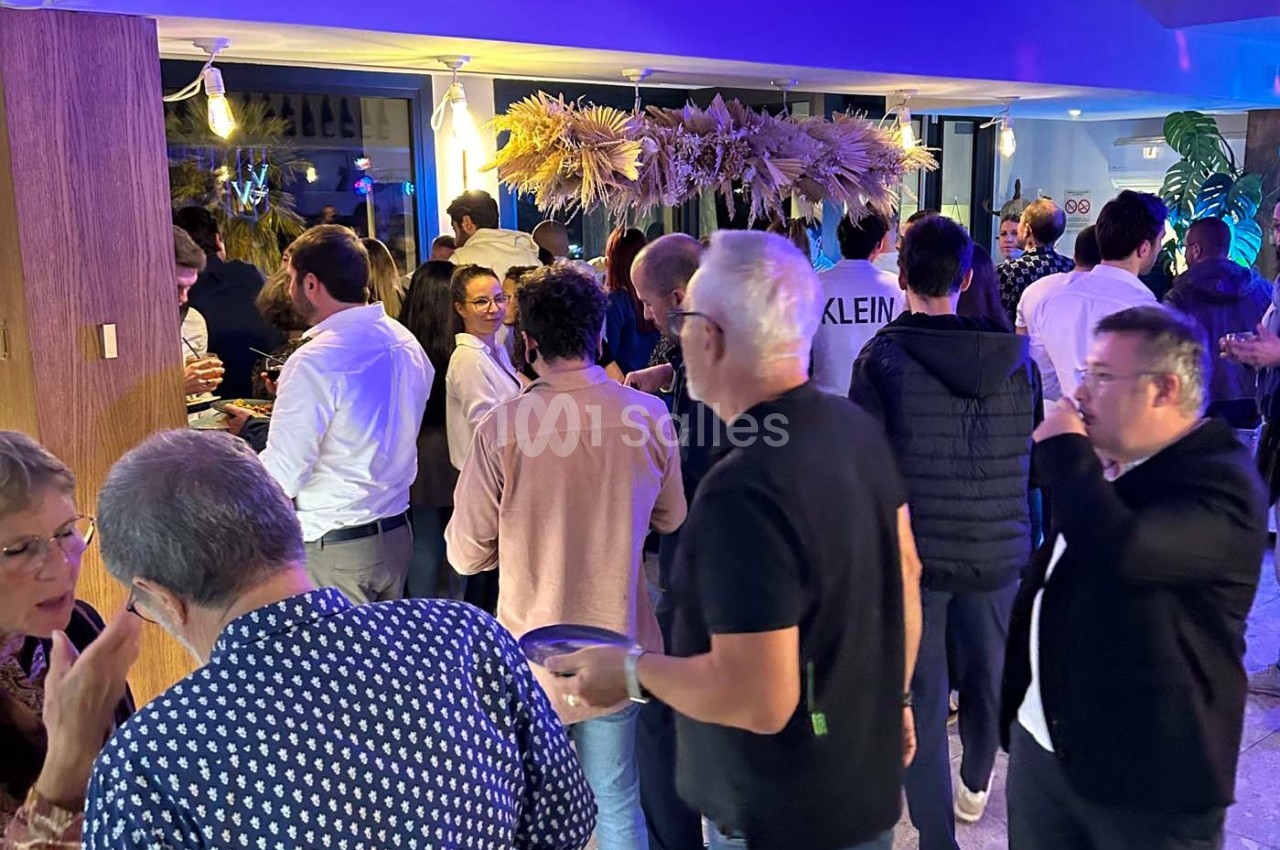 Groupe de personnes discutant et partageant un moment convivial dans un espace intérieur décoré de plantes et lumières.