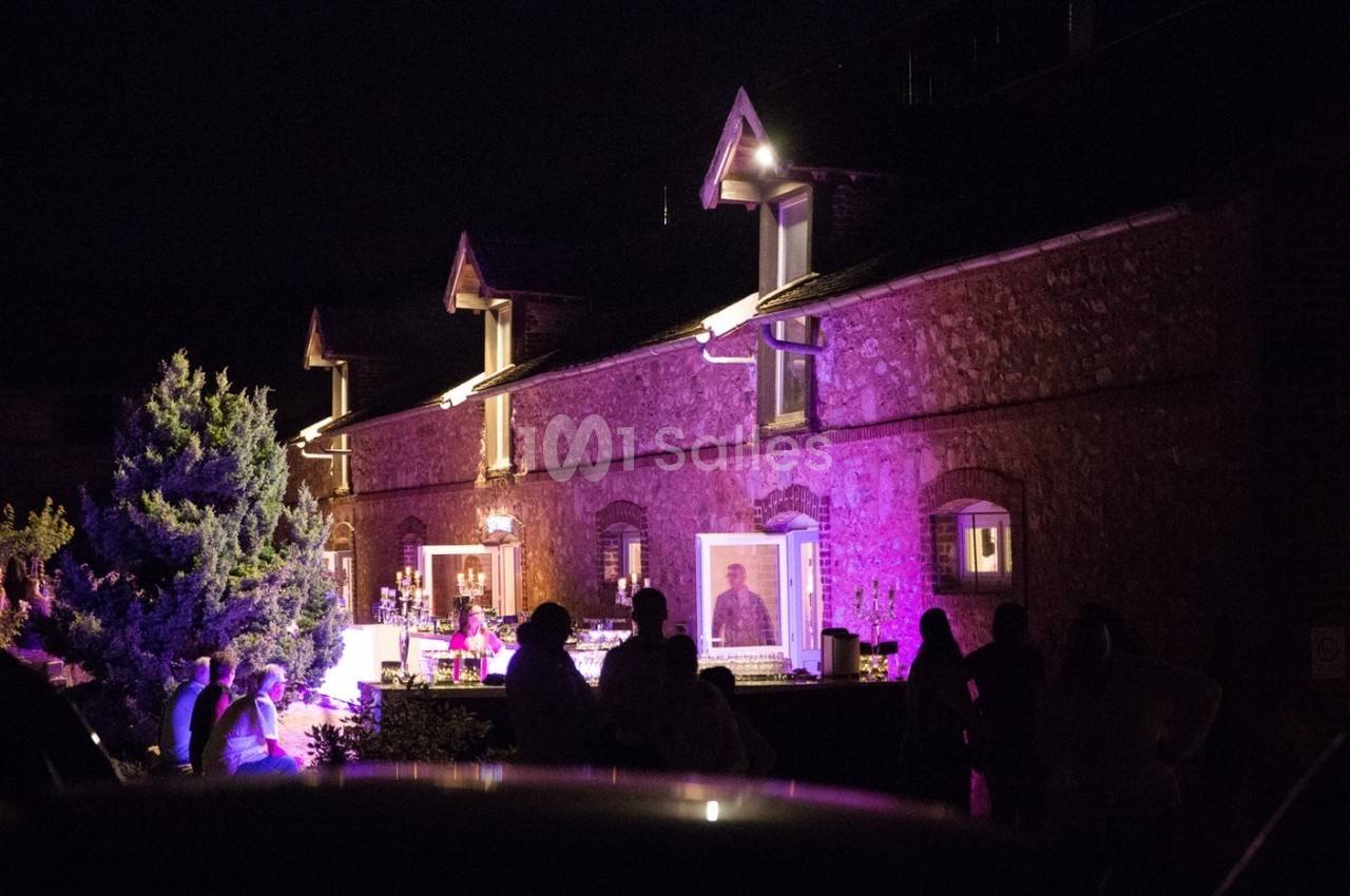 Façade en pierre éclairée par des lumières violettes, avec des silhouettes de personnes rassemblées devant.