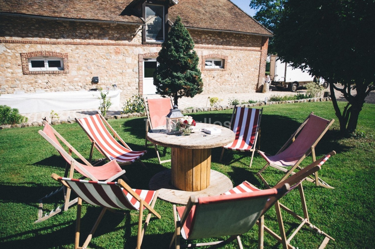 Chaises longues disposées en cercle autour d'une table en bois dans un jardin devant une maison en pierre.