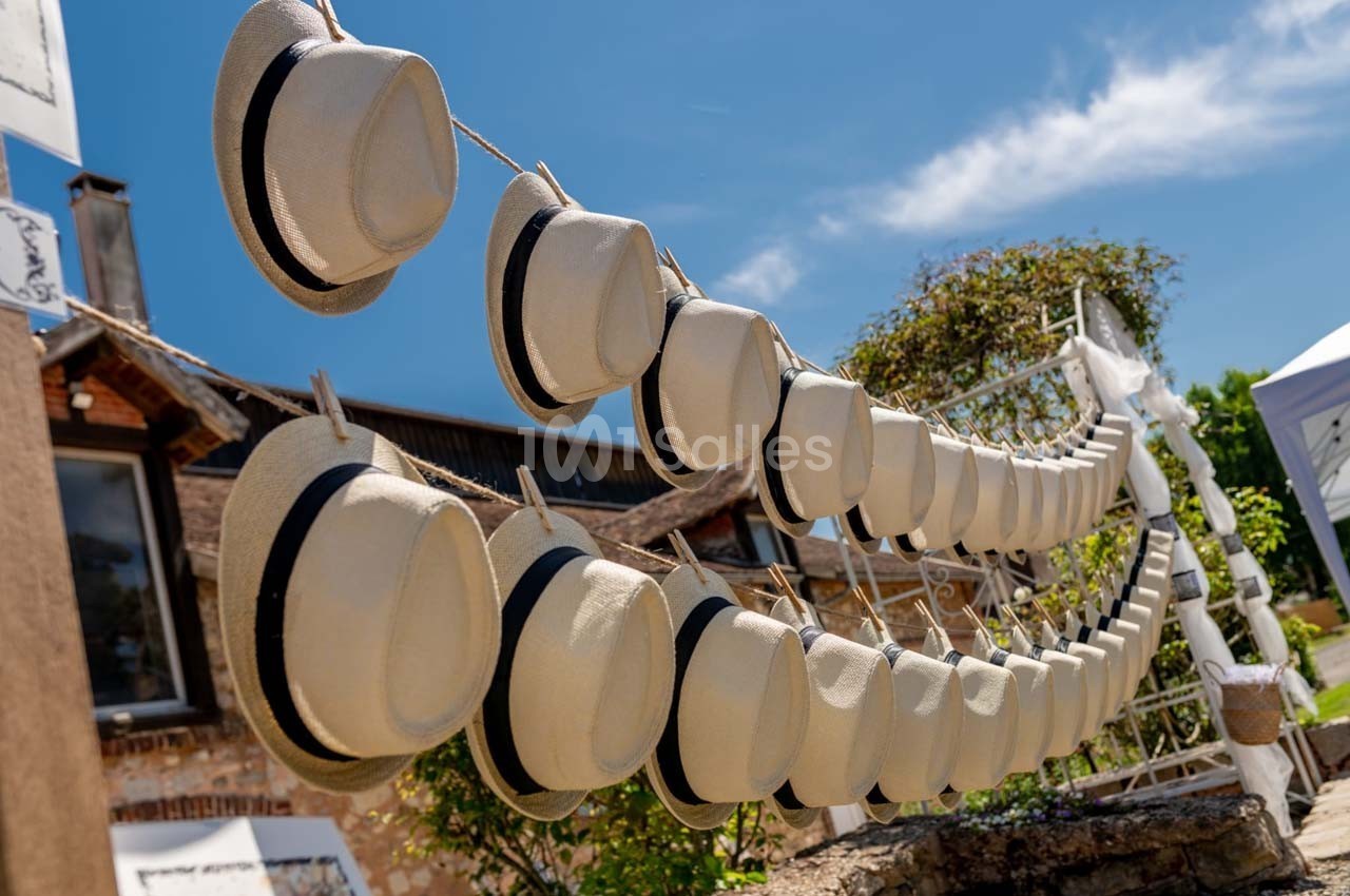 Chapeaux en paille beige suspendus sur des cordes en extérieur, sous un ciel bleu dégagé.