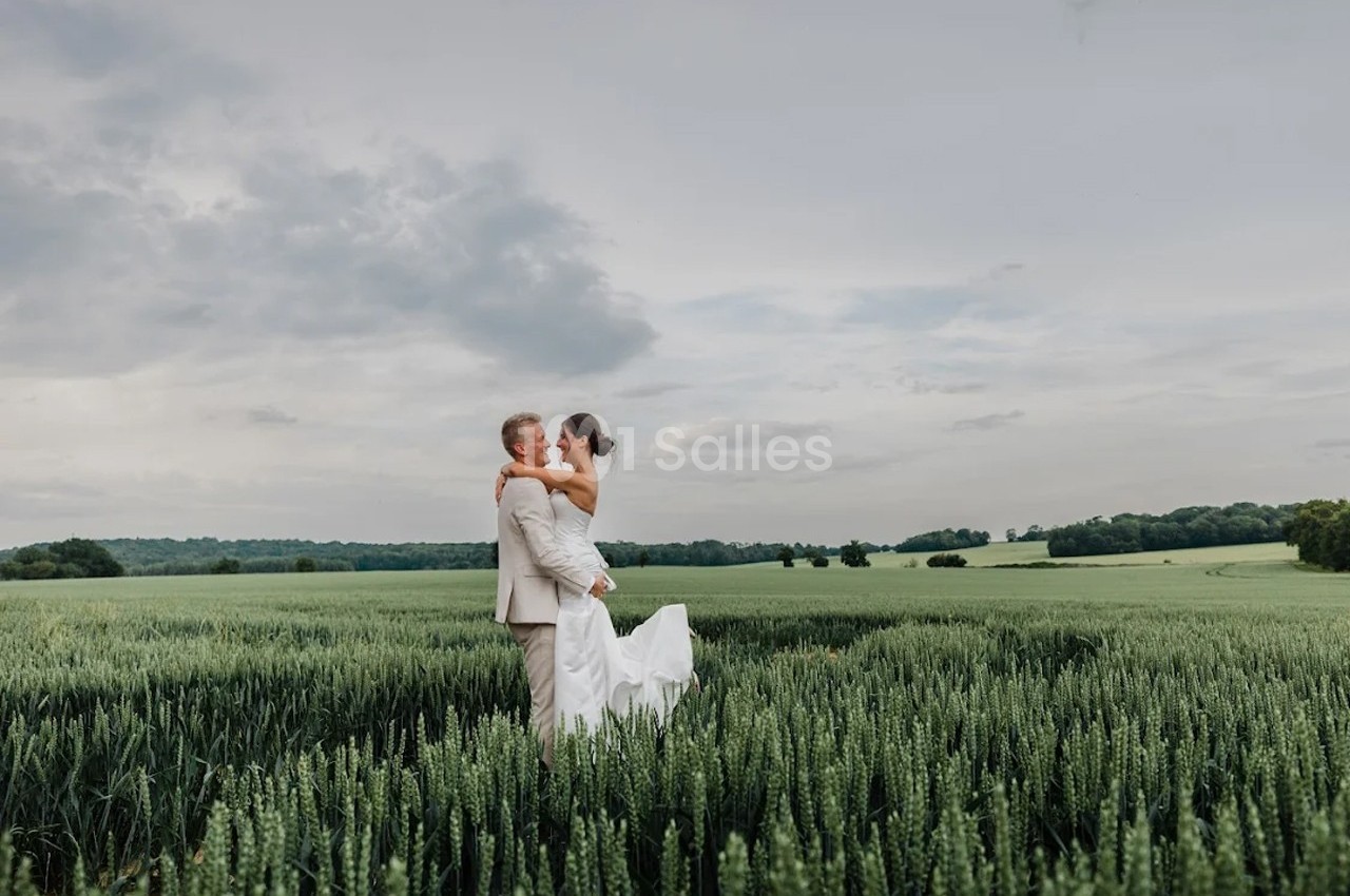 Un couple en tenue de mariage se tient dans un champ verdoyant sous un ciel nuageux.