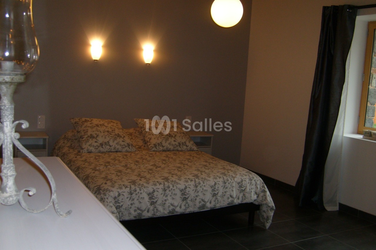 Chambre avec un lit double, éclairage mural, lampe suspendue, rideaux sombres et mur peint en gris.