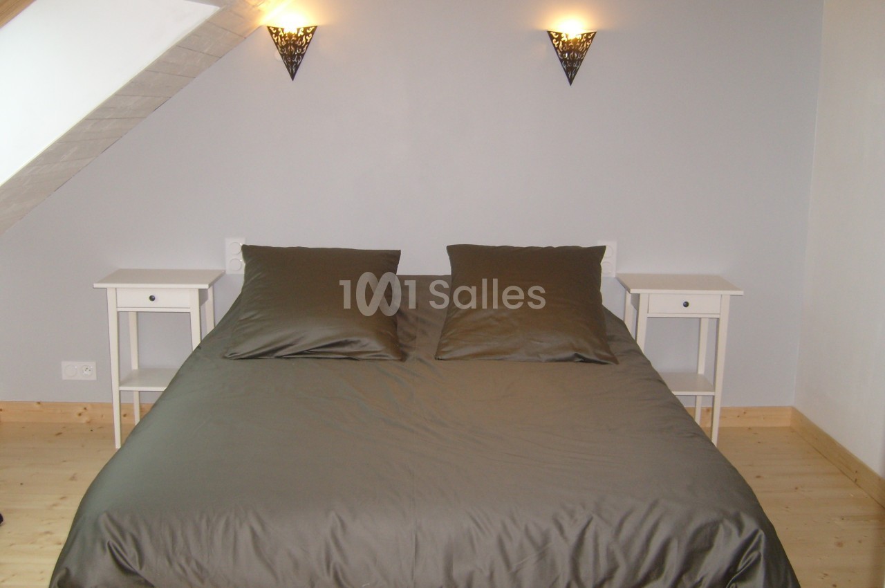 Lit double avec draps gris foncé, encadré par deux tables de chevet blanches et éclairé par deux appliques murales.