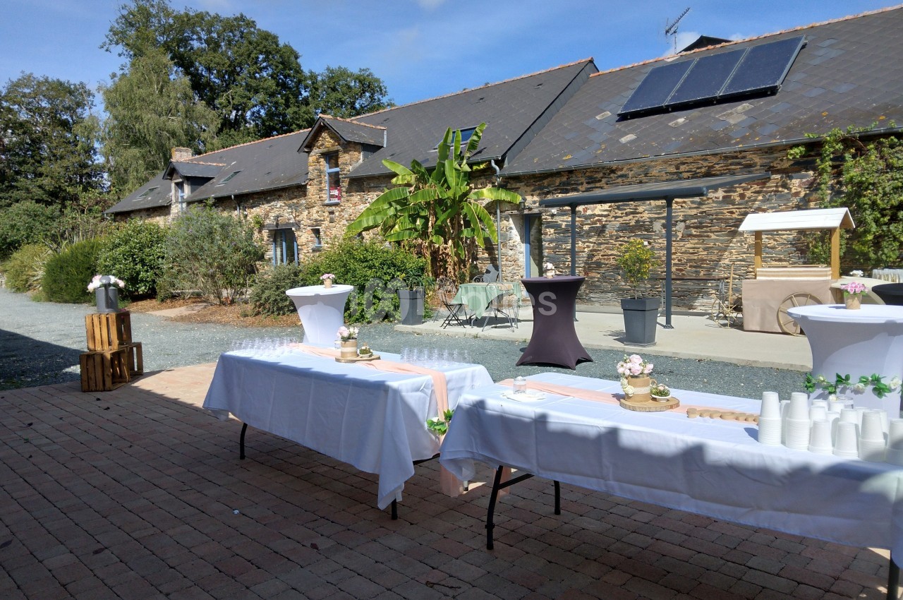 Tables dressées en extérieur avec nappes blanches devant un bâtiment en pierre sous un ciel dégagé.
