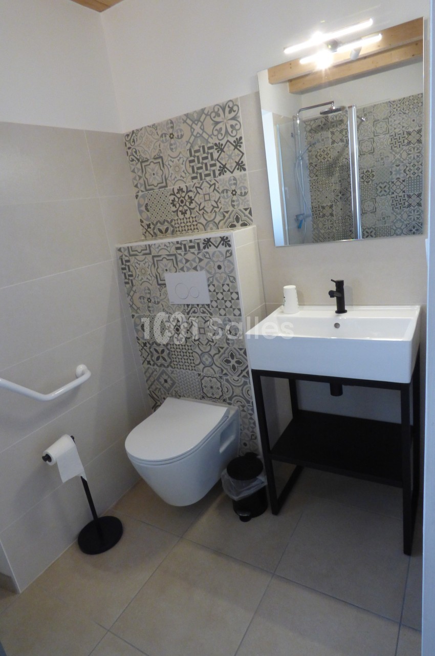 Salle de bain avec toilettes, lavabo sur meuble noir, carrelage décoratif et barre d'appui murale.