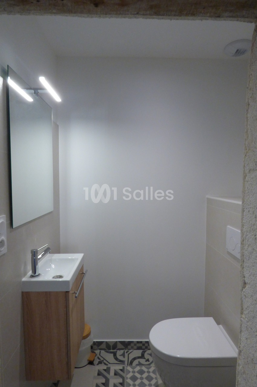 Salle de bain compacte avec lavabo en bois, miroir éclairé, toilettes blanches et carrelage à motifs au sol.
