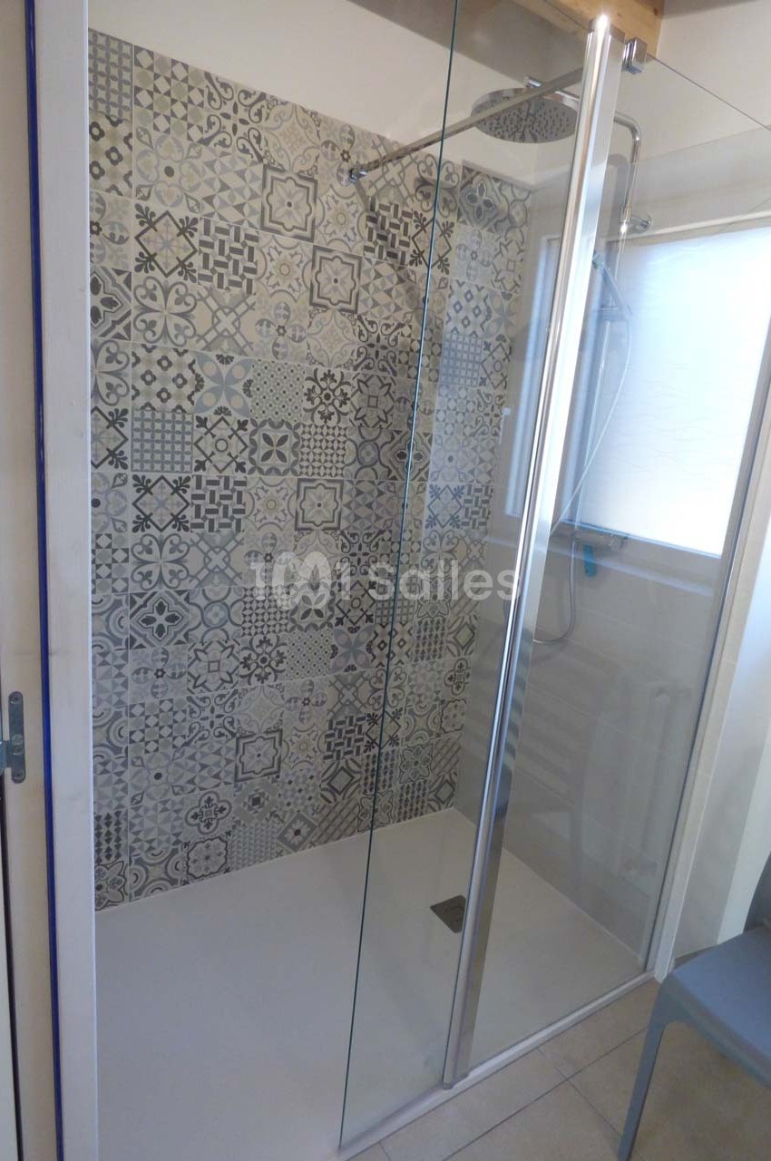 Douche à l'italienne avec parois vitrées, carrelage à motifs géométriques et fenêtre apportant de la lumière naturelle.