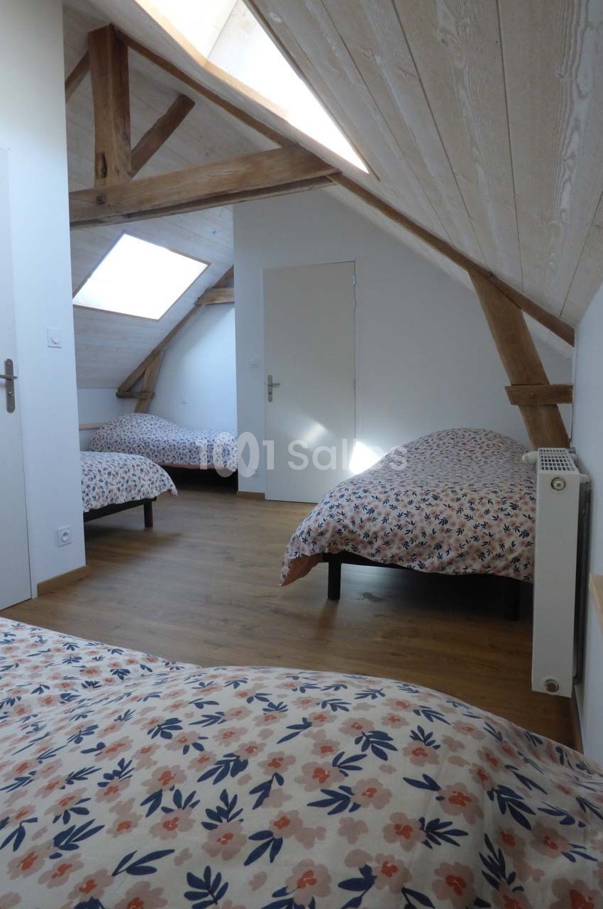 Chambre mansardée avec trois lits simples, parquet en bois clair, poutres apparentes et lumière naturelle.