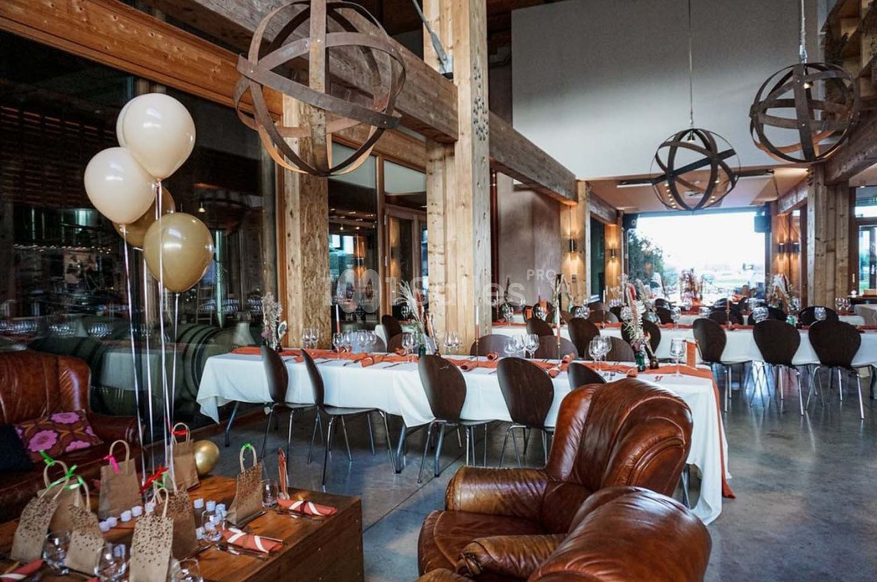 Salle de réception lumineuse avec tables dressées, décorations en bois et ballons beige et doré.