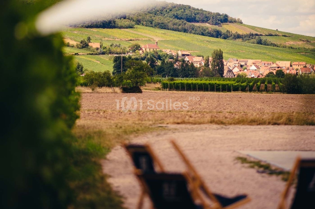 Village entouré de vignes et de collines verdoyantes, avec des chaises longues floues au premier plan.