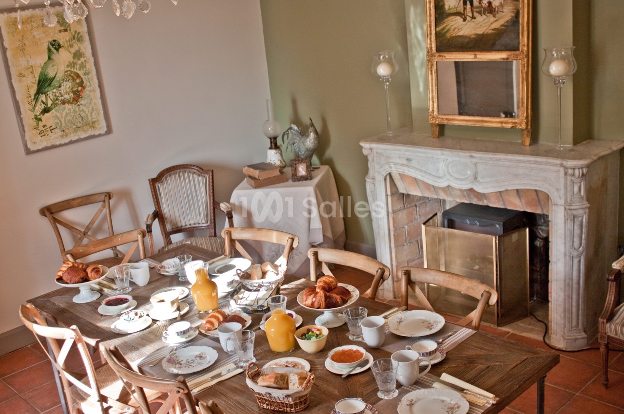 Table dressée pour un petit-déjeuner avec viennoiseries, jus d'orange et vaisselle, dans une salle à manger lumineuse.