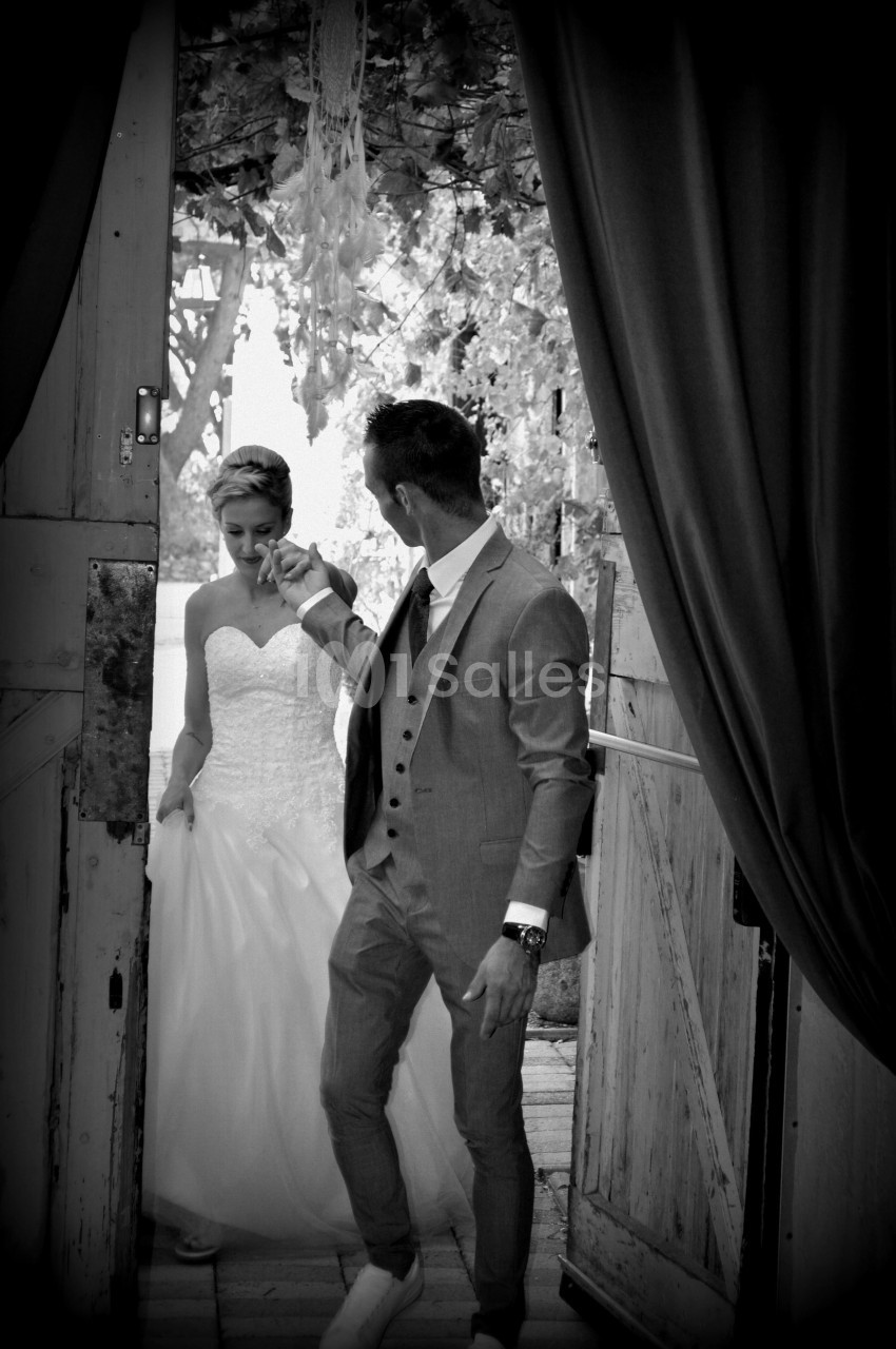 Un couple en tenue de mariage entre par une porte en bois, entouré de décorations florales.