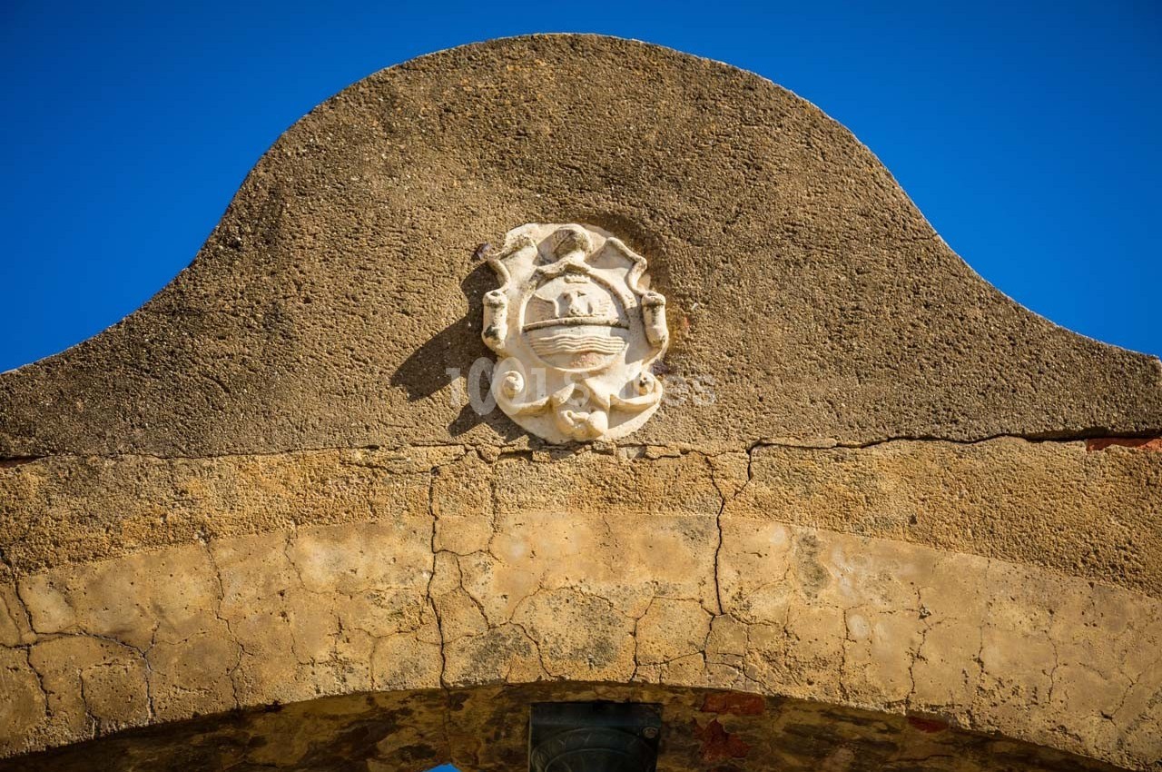 Détail d'un blason sculpté sur une arche en pierre ancienne, sous un ciel bleu clair.