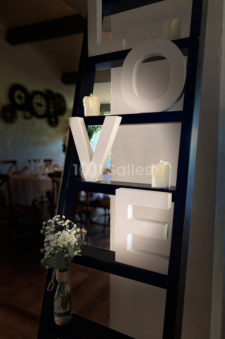 Étagère noire décorative avec le mot ’LOVE’ en lettres blanches, bougies et vase de fleurs blanches au premier plan.