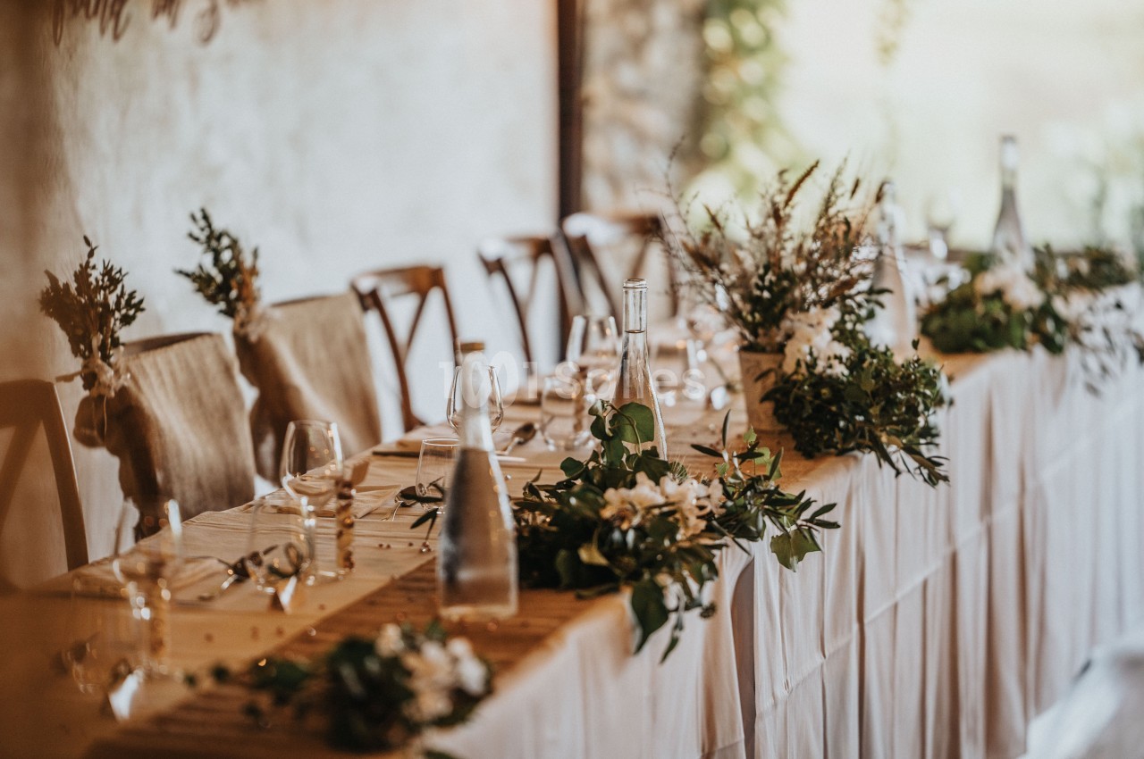 Table décorée pour un événement avec nappes blanches, chaises en bois, bouquets de fleurs et bouteilles en verre.