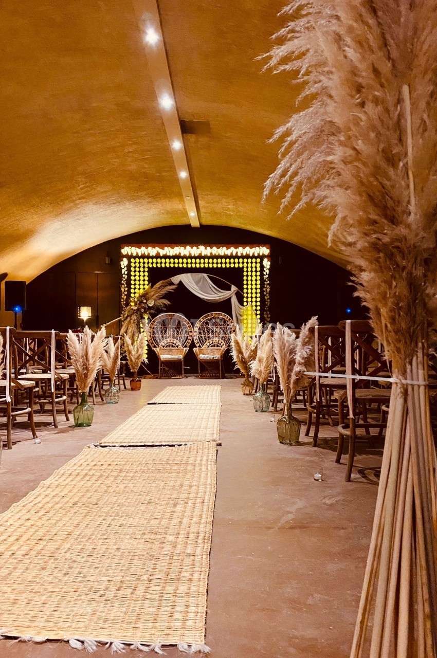 Allée décorée de tapis et de pampas menant à une arche lumineuse dans une salle voûtée.
