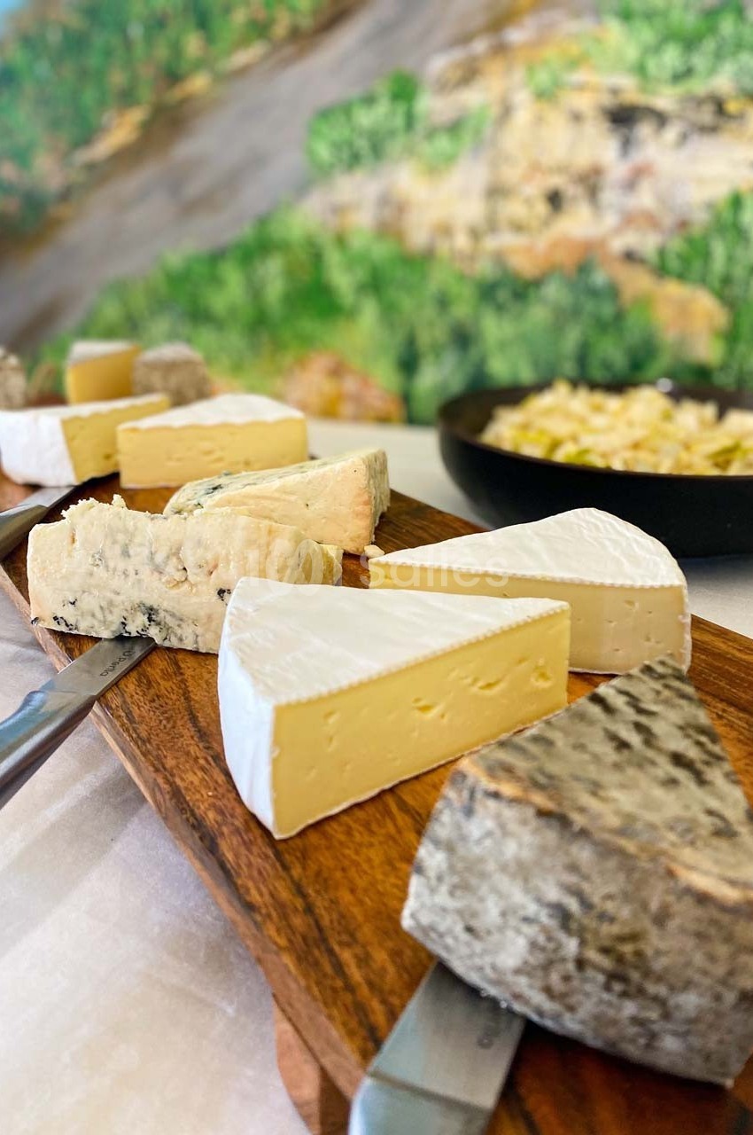 Plateau en bois avec divers fromages, dont des fromages à pâte molle et à croûte fleurie, présenté sur une table.
