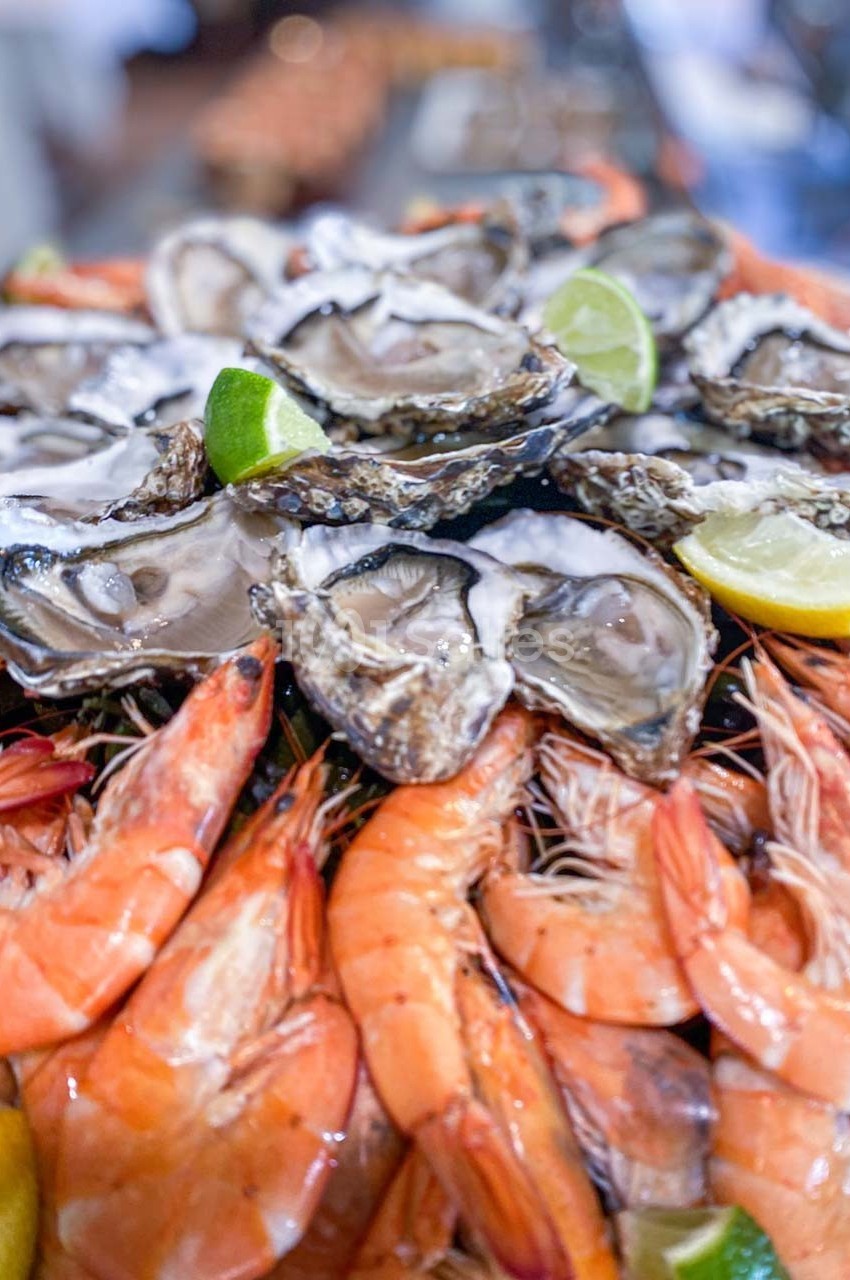 Plateau de fruits de mer avec huîtres ouvertes, crevettes et quartiers de citron vert et jaune.