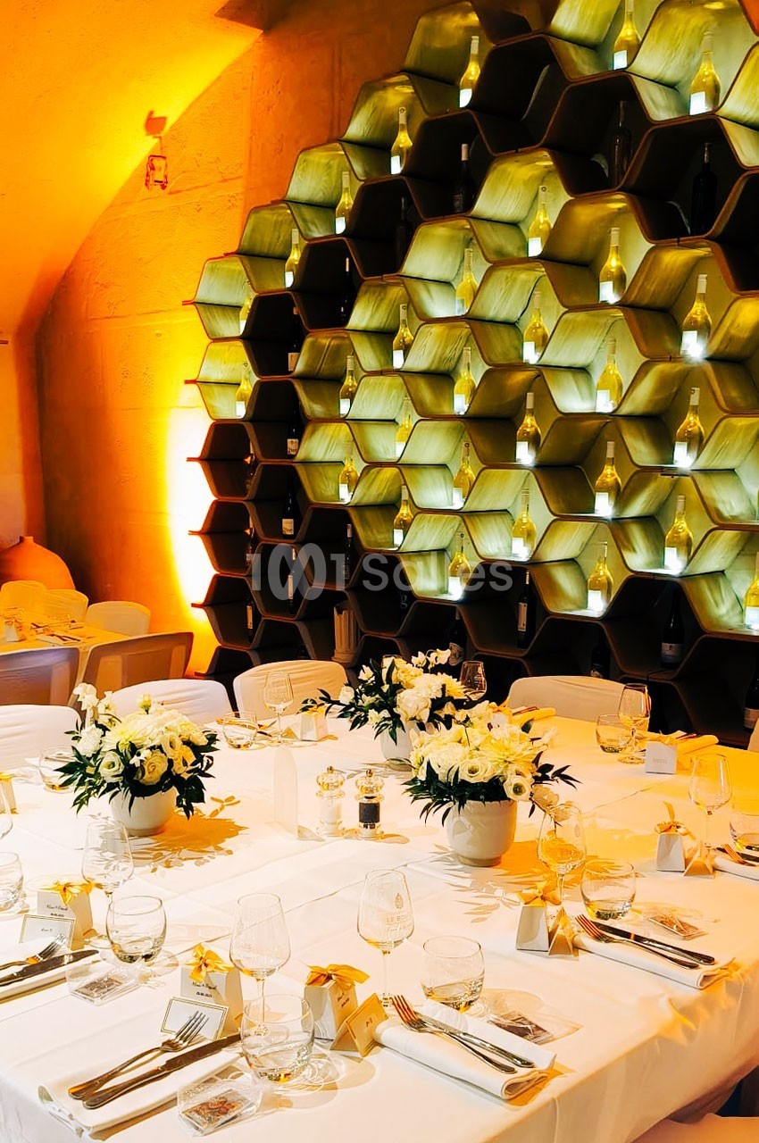 Tables élégamment dressées avec des fleurs blanches devant un mur décoratif en forme de rayons de miel illuminés.