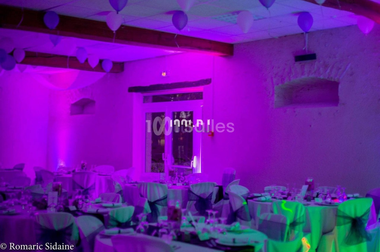 Salle de réception décorée avec des tables dressées, des ballons suspendus et un éclairage violet.