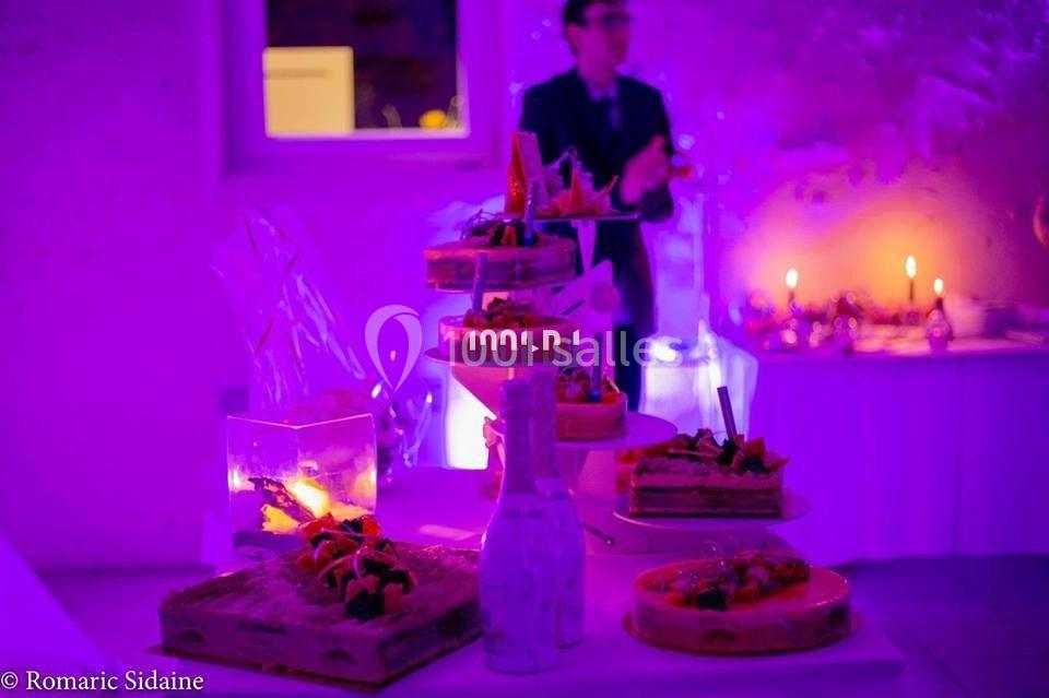 Plateau de desserts variés sur une table éclairée par une lumière violette, avec un homme flou en arrière-plan.
