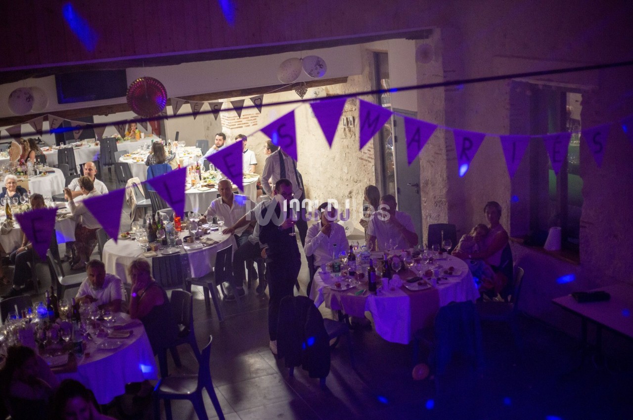 Salle de réception décorée avec des guirlandes, des invités assis à des tables rondes pendant un événement festif.