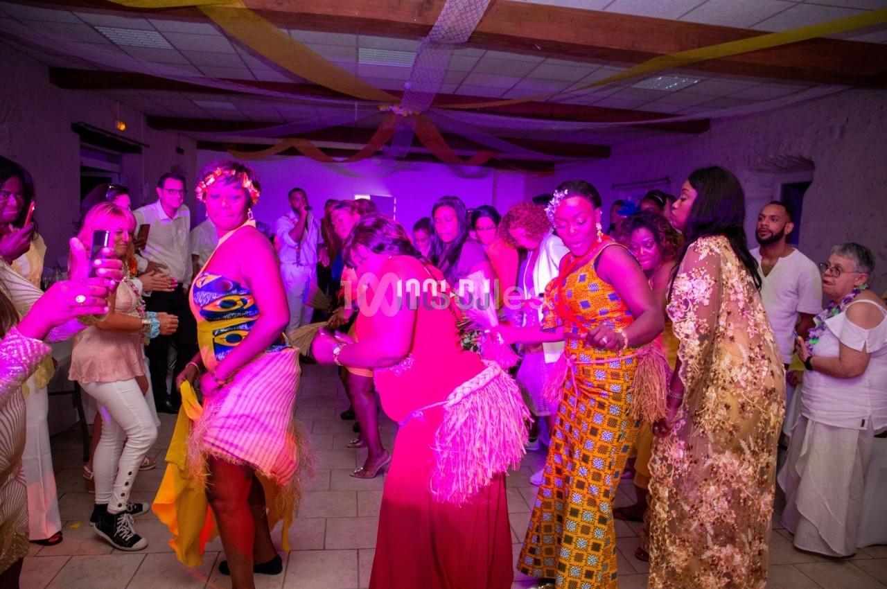 Des personnes dansent lors d'une fête dans une salle décorée avec des guirlandes et un éclairage coloré.