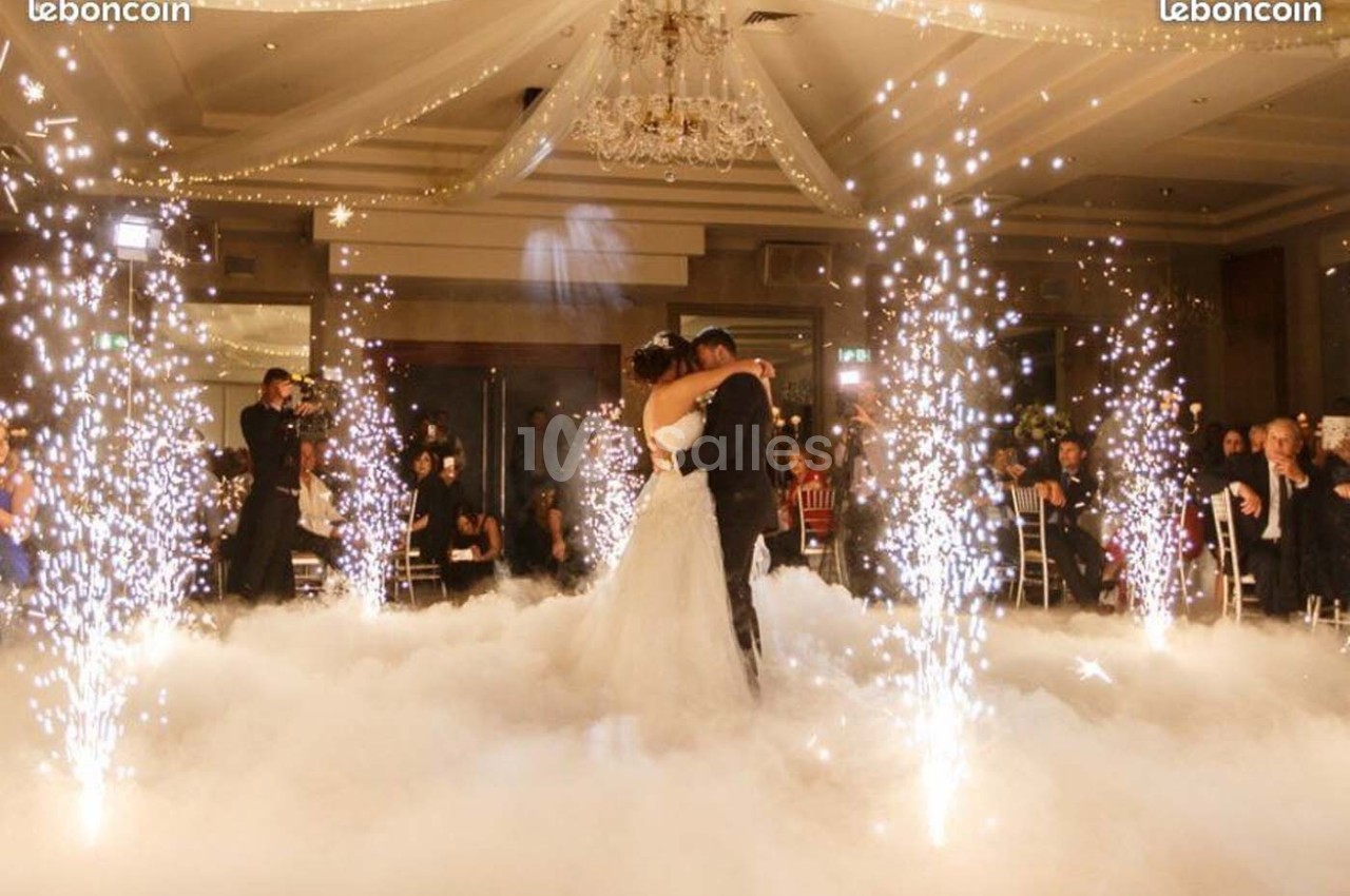 Un couple danse au milieu d'une piste entourée de fumée et de jets d'étincelles dans une salle décorée.