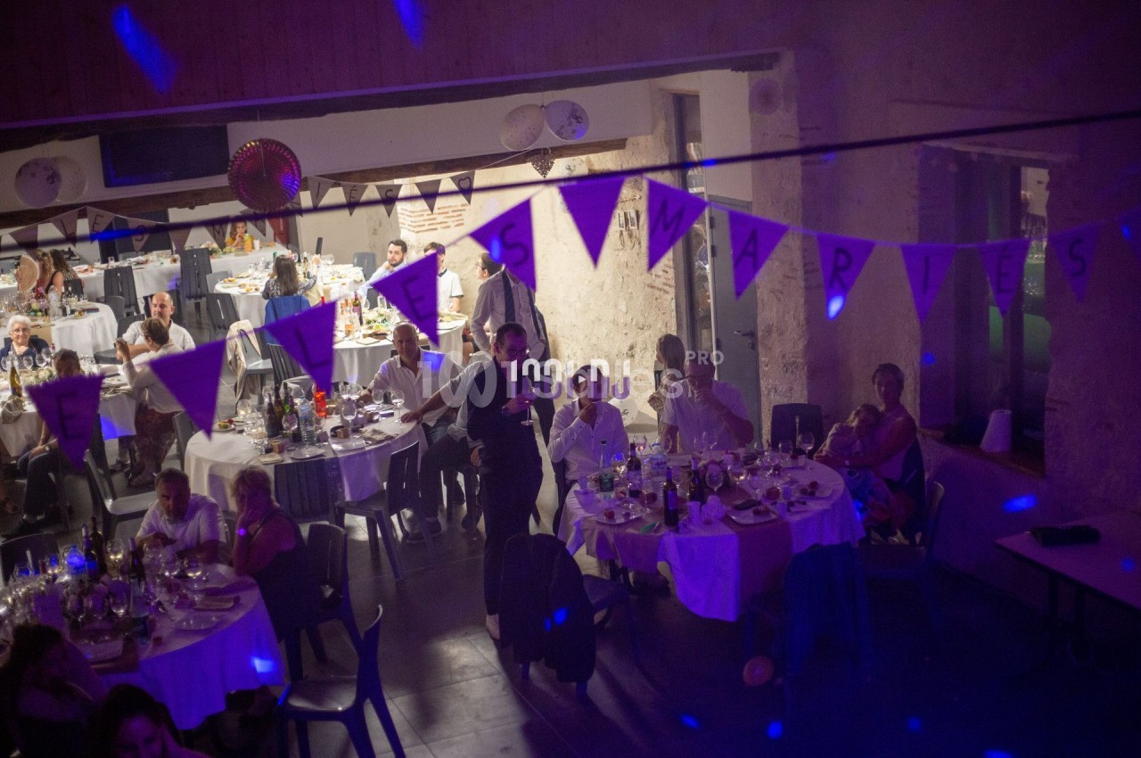 Salle de réception décorée avec des guirlandes, des invités assis à des tables rondes pendant un événement festif.