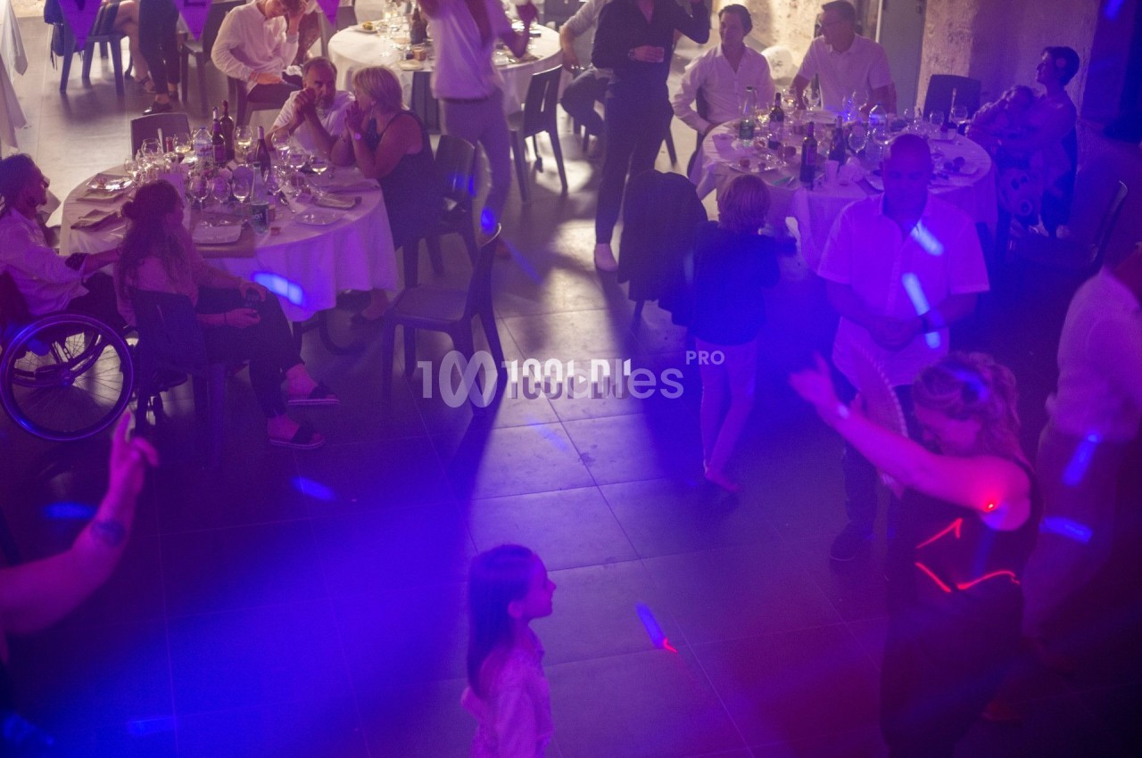 Des personnes dansent sous des lumières colorées dans une salle de réception avec des tables dressées en arrière-plan.