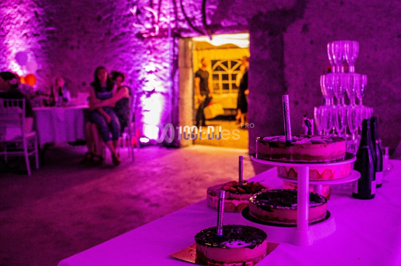 Des desserts disposés sur une table blanche dans une salle éclairée par des lumières violettes, avec des invités en arrière…