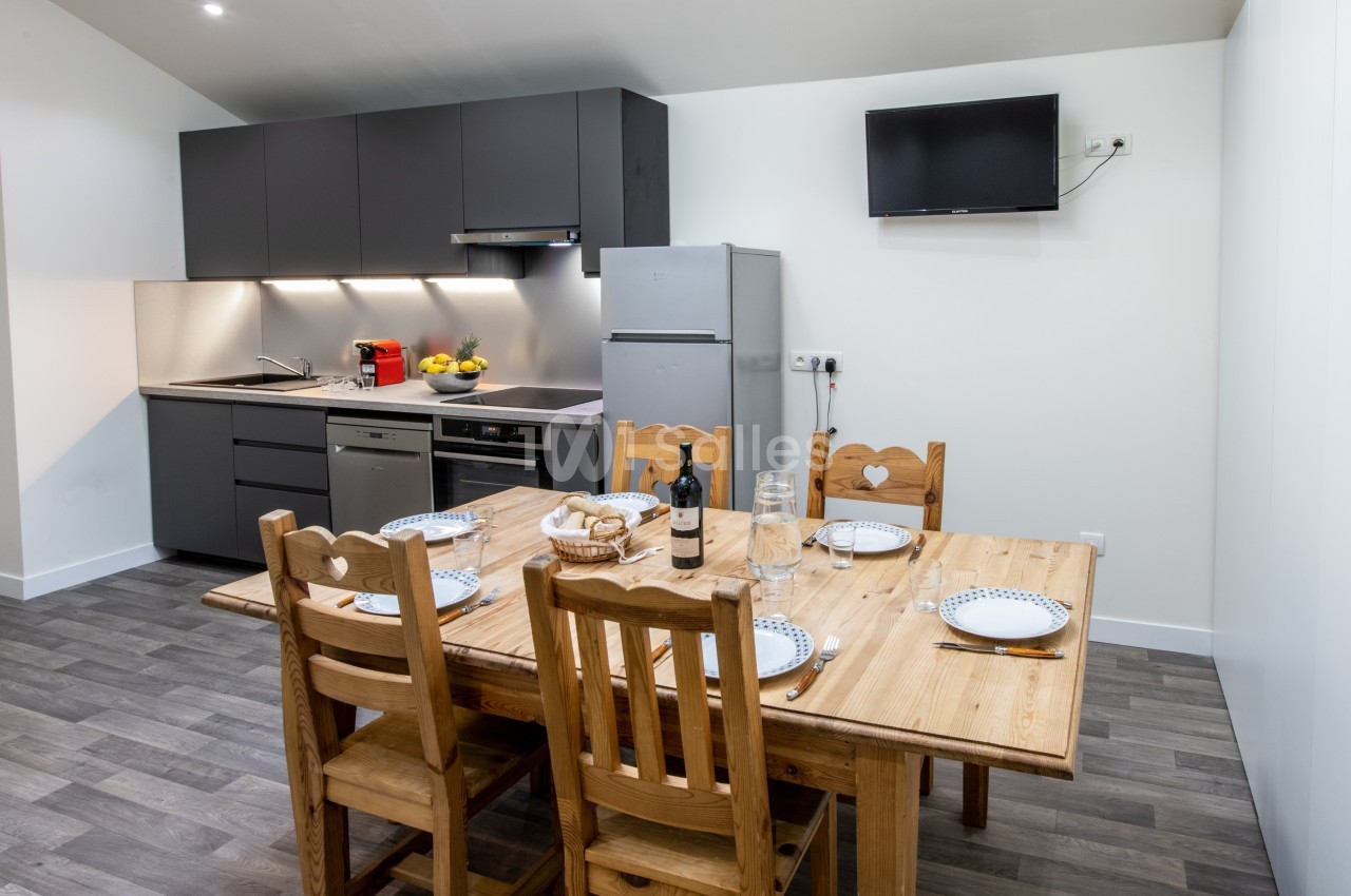 Cuisine moderne avec table en bois dressée pour quatre personnes, équipée d'appareils électroménagers et d'une télévision…