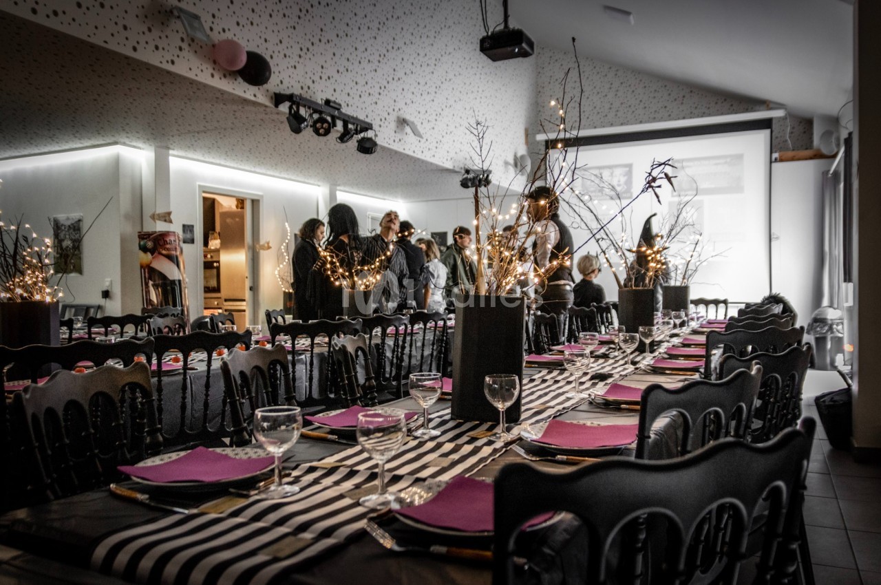 Salle décorée pour un événement, avec tables dressées, nappes rayées, et centres de table lumineux.