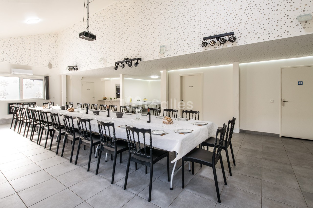 Salle lumineuse avec une grande table dressée pour un repas, entourée de chaises noires, dans un décor moderne.