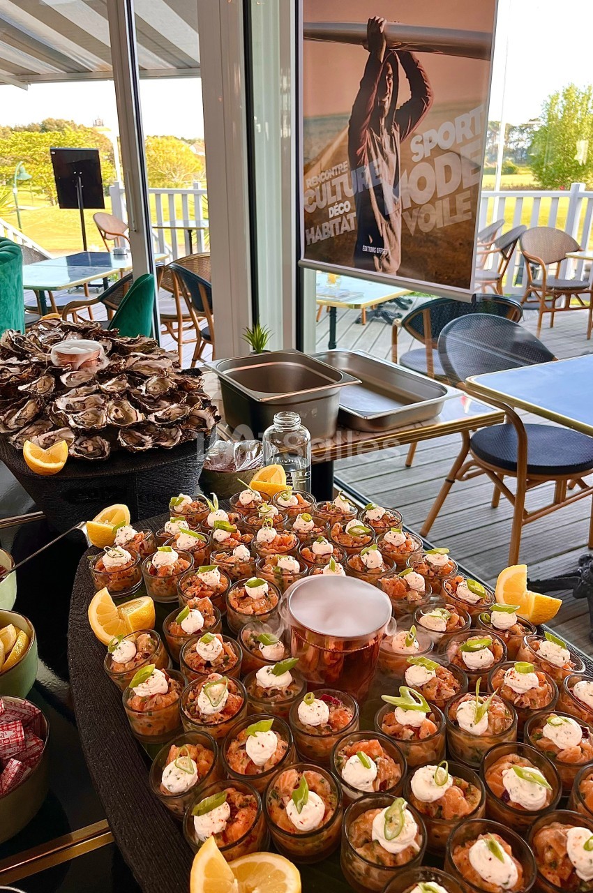 Buffet avec verrines de crevettes, huîtres et citrons, installé dans une salle lumineuse avec vue sur une terrasse.
