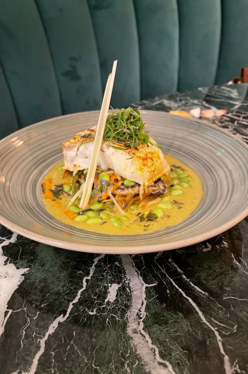 Plat de poisson blanc sur un lit de légumes et nouilles dans une sauce crémeuse, servi dans une assiette sur une table en…