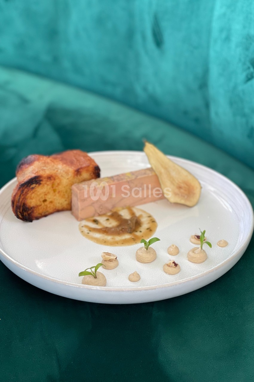 Assiette avec un bloc de foie gras, tranche de pain brioché, poire pochée et décorations de crème et noisettes.